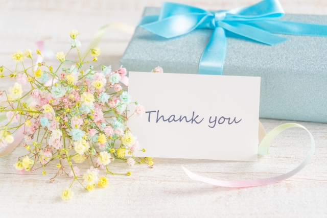 パステルカラーのカスミソウとブルーのラッピングのプレゼントと「Thank you」カード